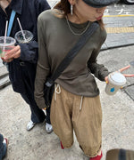 グレーのアウトシームロングTシャツとベージュのバルーンパンツを着用し、屋外の歩道に立っている人物。手にはドリンクを持っている。