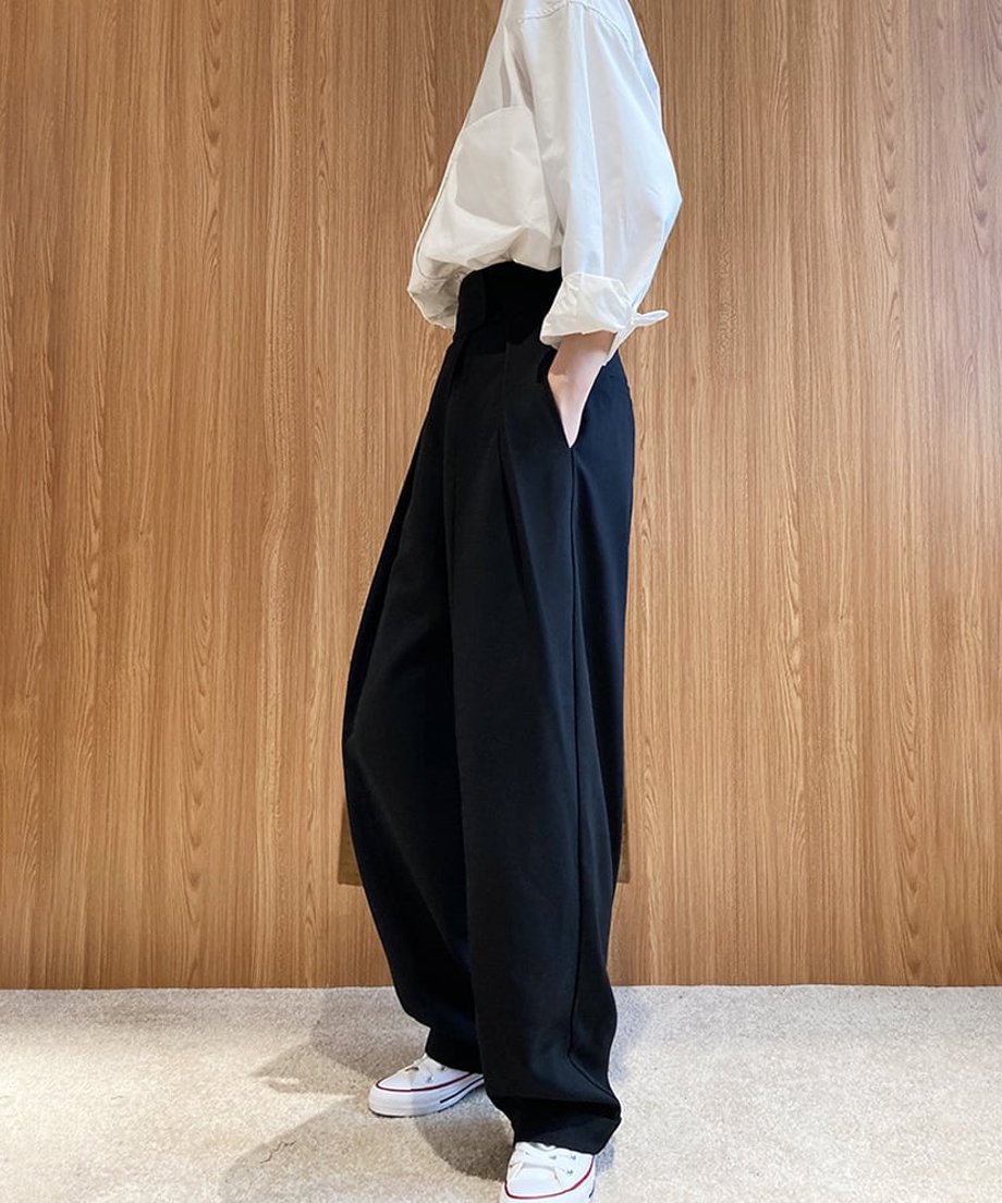 ブラックのハイウエストワイドタックパンツを白いシャツに合わせたコーディネートの側面。パンツのボリューム感とスニーカーが確認できる。