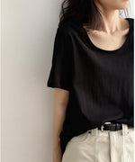 黒色のUネックTシャツを着用した女性の上半身。Tシャツをベージュのパンツにタックインし、黒いベルトを締めている。