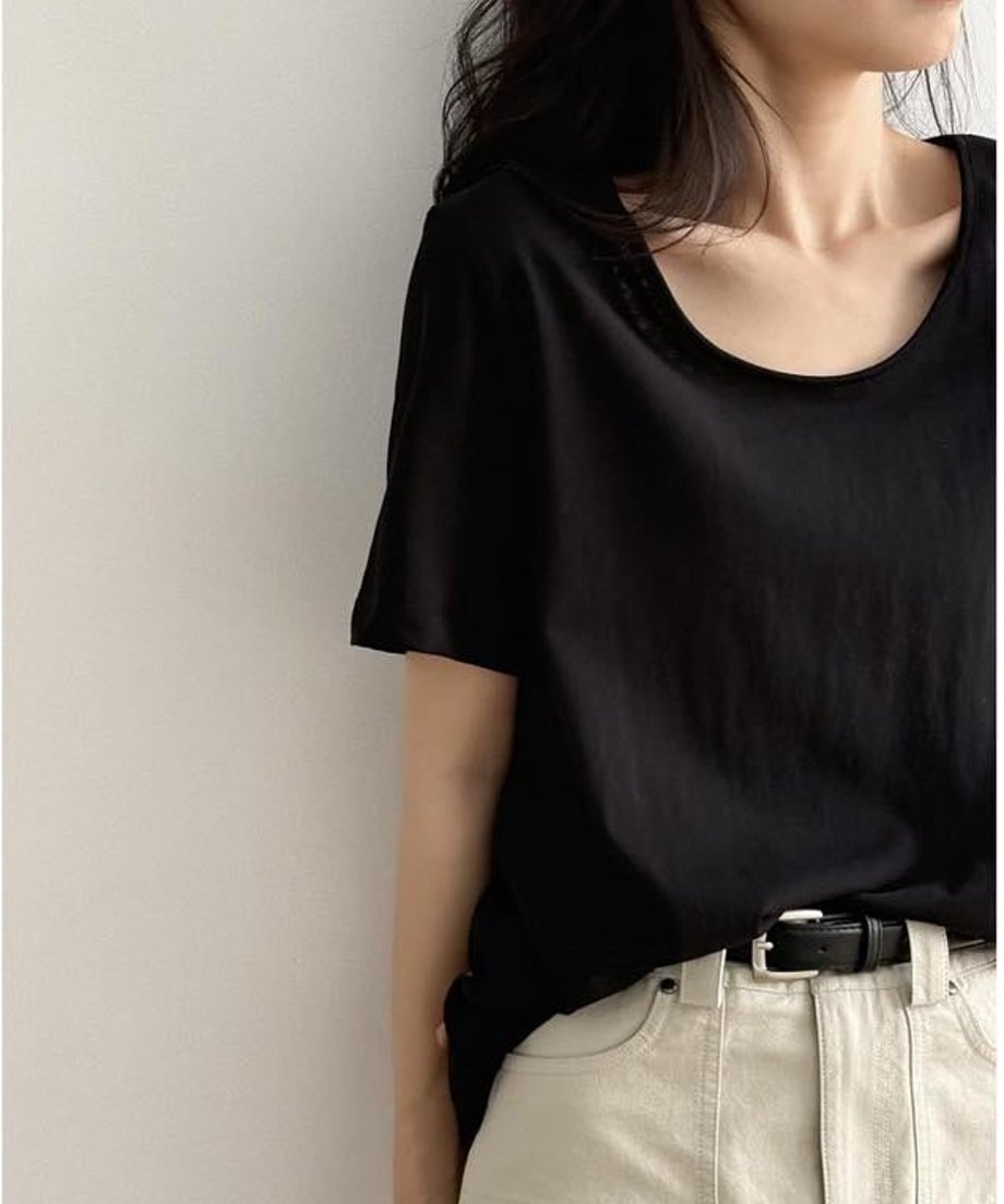 黒色のUネックTシャツを着用した女性の上半身。Tシャツをベージュのパンツにタックインし、黒いベルトを締めている。