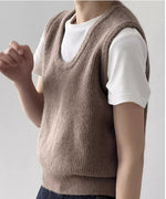 ベージュのUネックニットベストを白Tシャツと濃い色のデニムにレイヤードし着用している女性のクローズアップ。