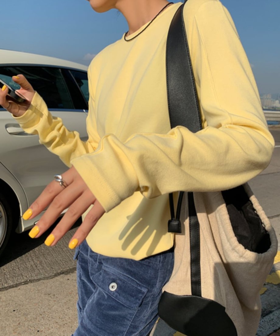 イエローのアウトシームロングTシャツを着て、ネイビーのコーデュロイカーゴパンツと合わせた人物のバストアップ。斜め掛けバッグを着用。