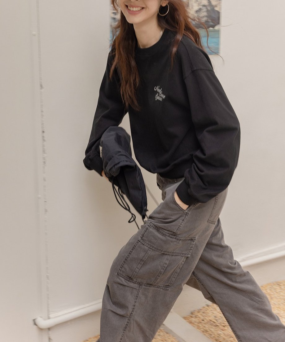 黒のスウェットを着用し、グレーのキャップと濃いグレーのデニムパンツを合わせた女性の動きのあるショット。胸には白いプリントロゴがある。