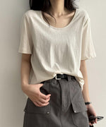 アプリコットのUネックTシャツを着用した女性の上半身。Tシャツをグレーのカーゴポケット付きミニスカートに軽くタックインしている。