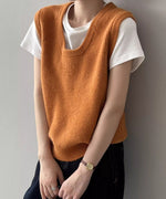 オレンジ色のUネックニットベストを白Tシャツと黒っぽいデニムにレイヤードし着用している女性のクローズアップ。