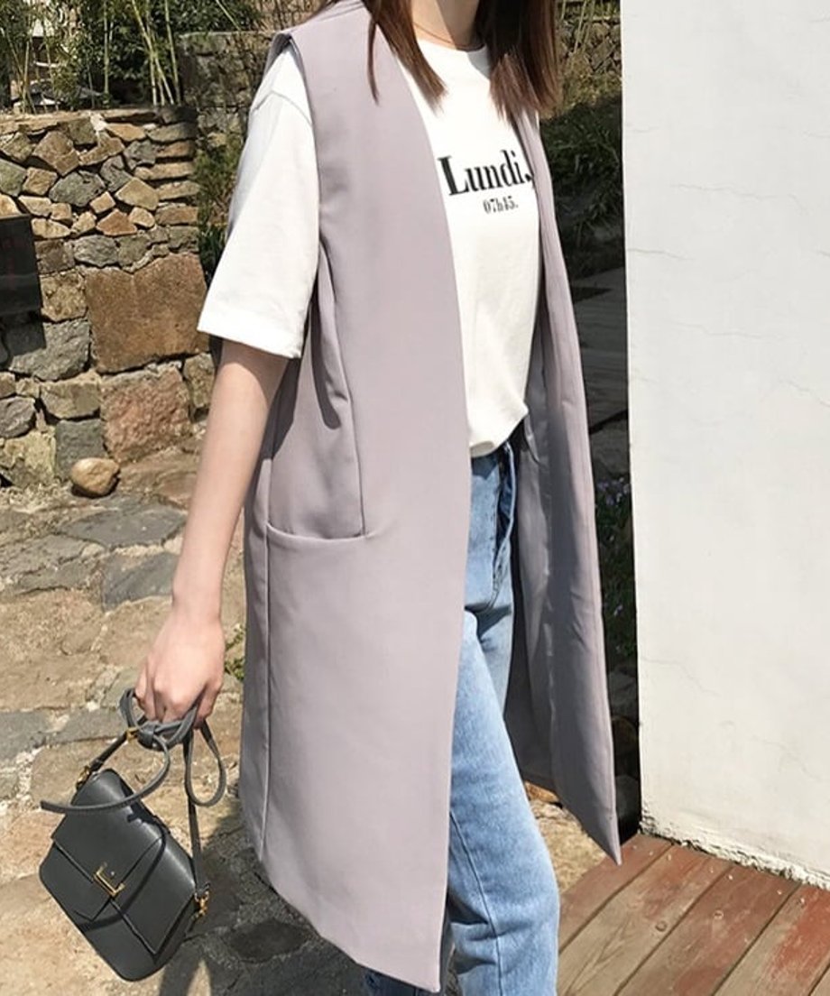 白いロゴTシャツとデニムにライトグレーのロングベストを羽織った女性。