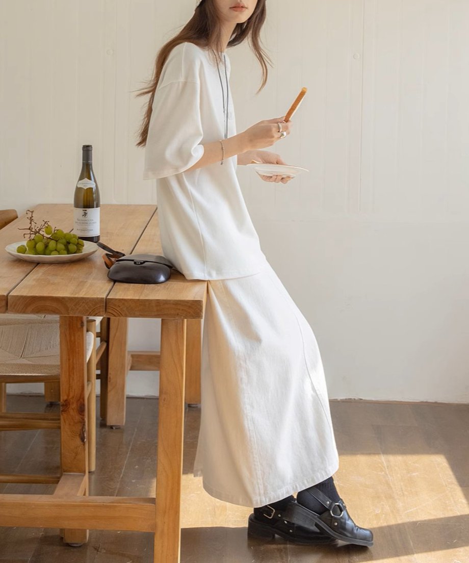 白いトップスとマキシスカートを着用し、テーブルに座っている女性。カジュアルな雰囲気。