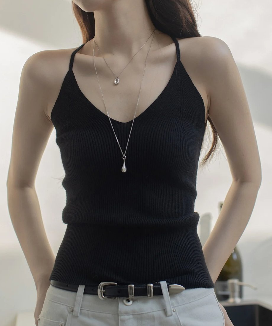 黒のリブ編みVネックキャミソールを着用した女性の半身。ライトベージュのパンツと黒いベルト、シルバーのネックレスを着用。