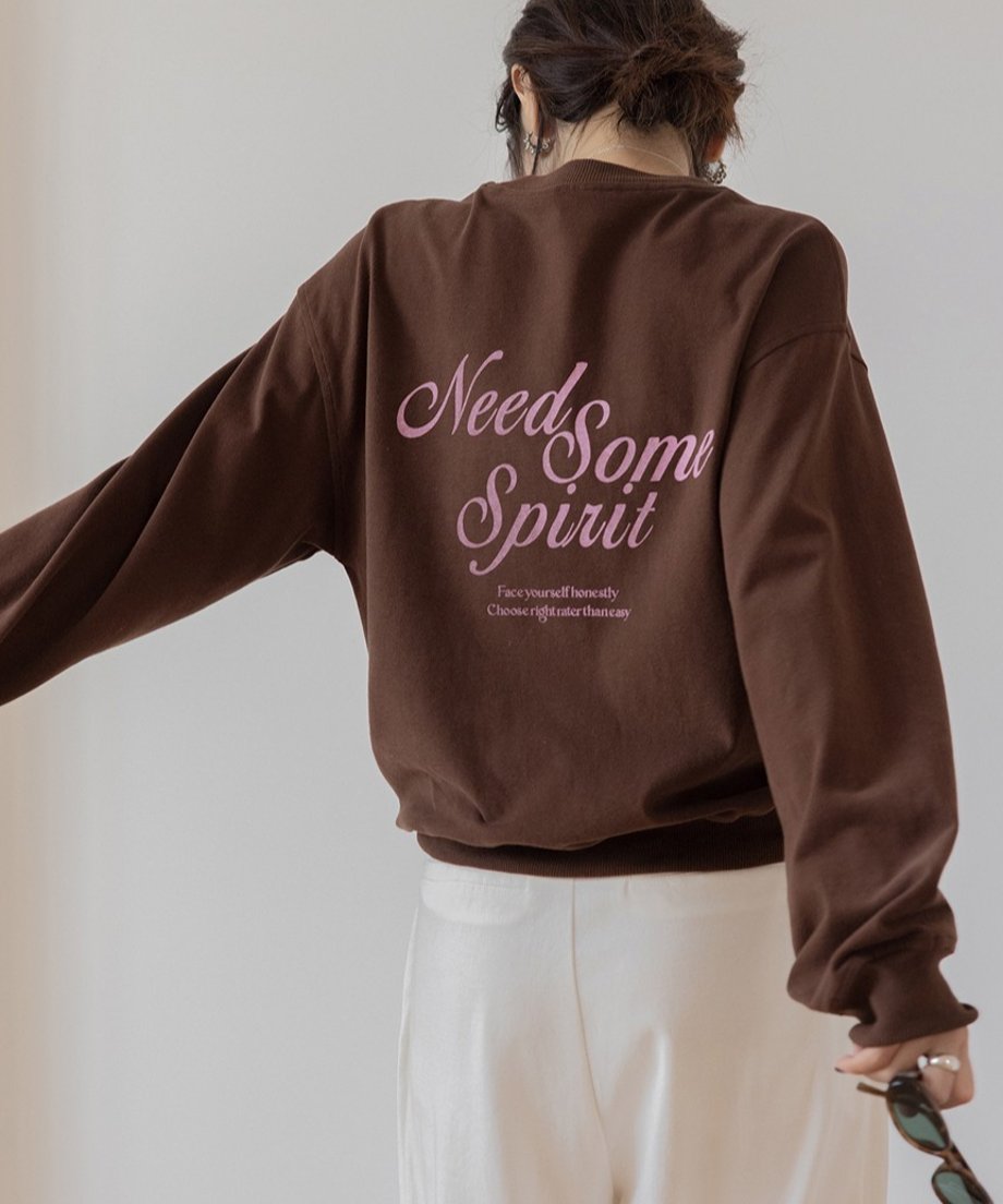 ブラウンのスウェットを着用した女性の背中のクローズアップ。胸元にピンク色の刺繍ロゴがある。