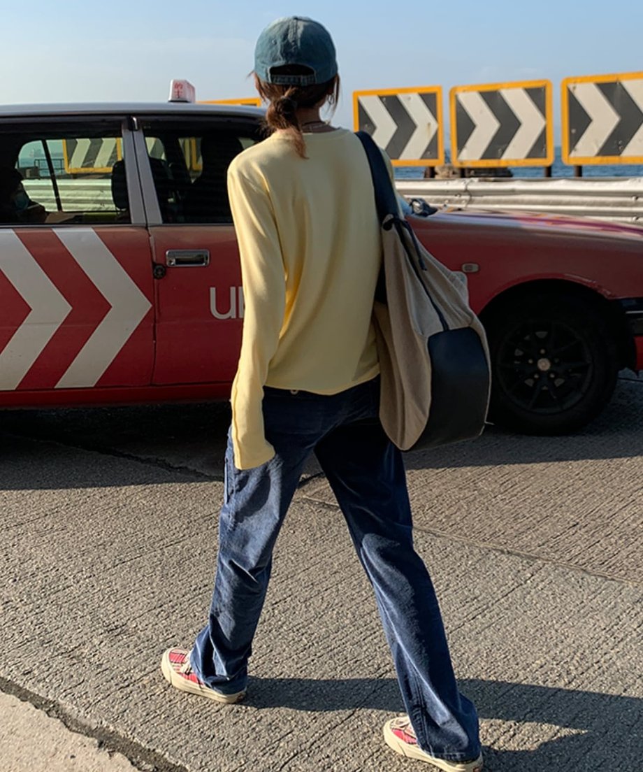 イエローのアウトシームロングTシャツを着て、濃いネイビーのデニムまたはコーデュロイパンツを着用した人物の後ろ姿。赤い車の前で撮影。