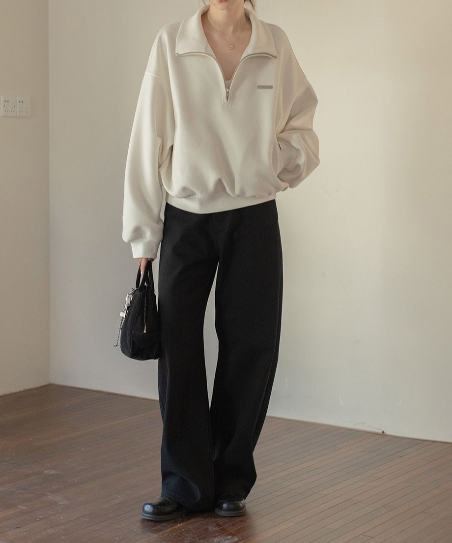 ホワイトのハーフジップトップスとブラックセミワイドパンツを着た屋外の人物。