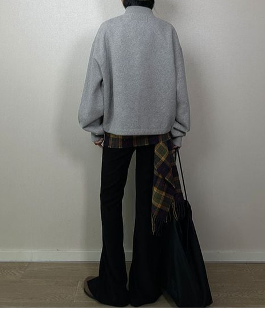 グレーのラージポケットブルゾンを着用した女性の後ろ姿。黒いフレアパンツと、チェック柄のシャツやスカーフをレイヤードしている。