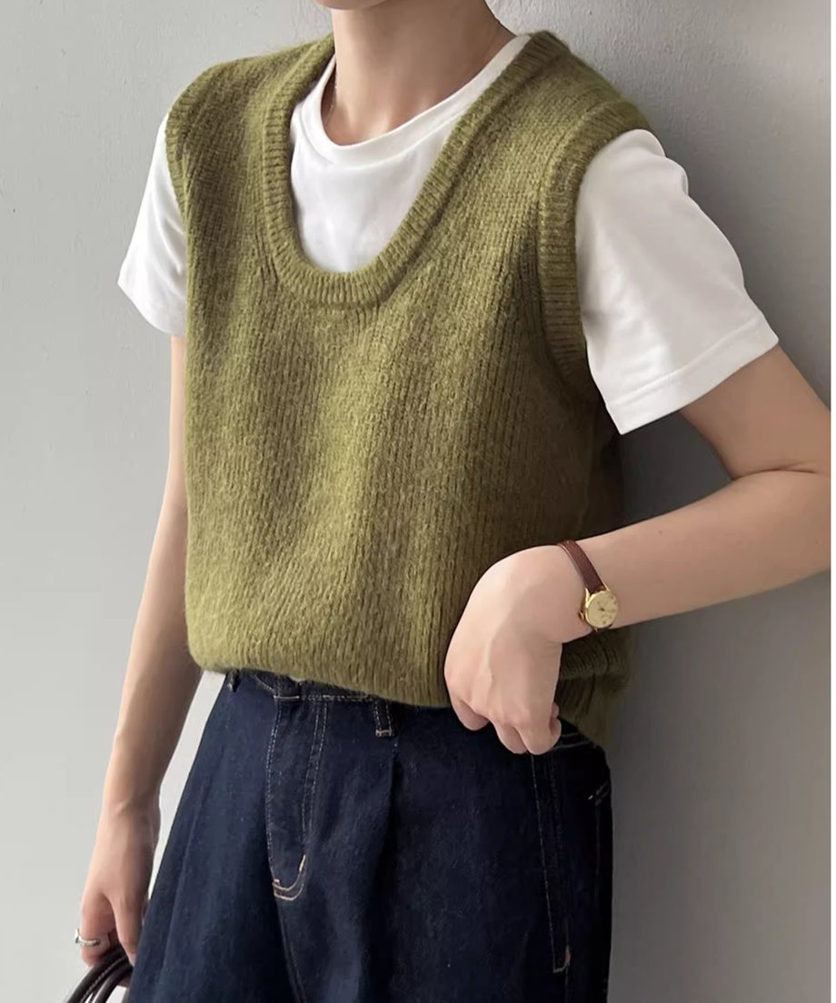 カーキのUネックニットベストを白Tシャツと濃い色のデニムにレイヤードして着用している女性のクローズアップ。