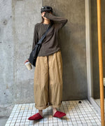 グレーのアウトシームのロングTシャツとベージュのワイドパンツを着用し、サングラスとキャップを被った人物の全身ショット。赤いサンダルを履いている。