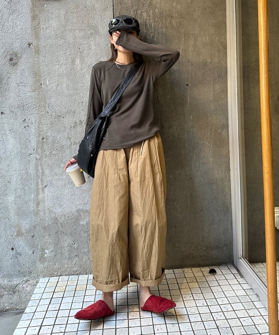 グレーのアウトシームのロングTシャツとベージュのワイドパンツを着用し、サングラスとキャップを被った人物の全身ショット。赤いサンダルを履いている。