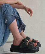デニムパンツをロールアップしブラックの厚底バックルサンダルを履いて座る女性の足元