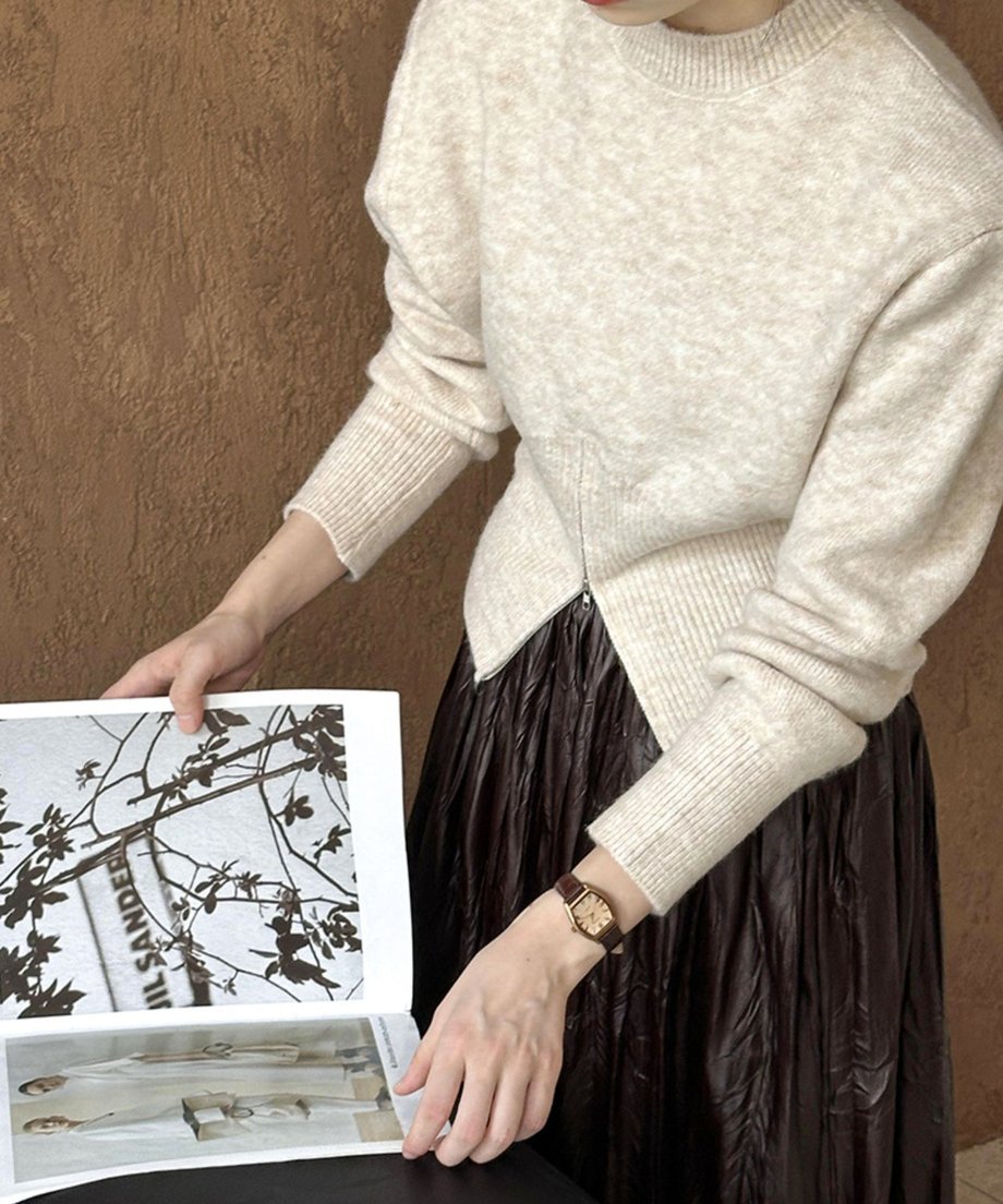 ベージュのハーフジップニットと茶色いレザースカートを着用した女性の半身像。雑誌を広げている。