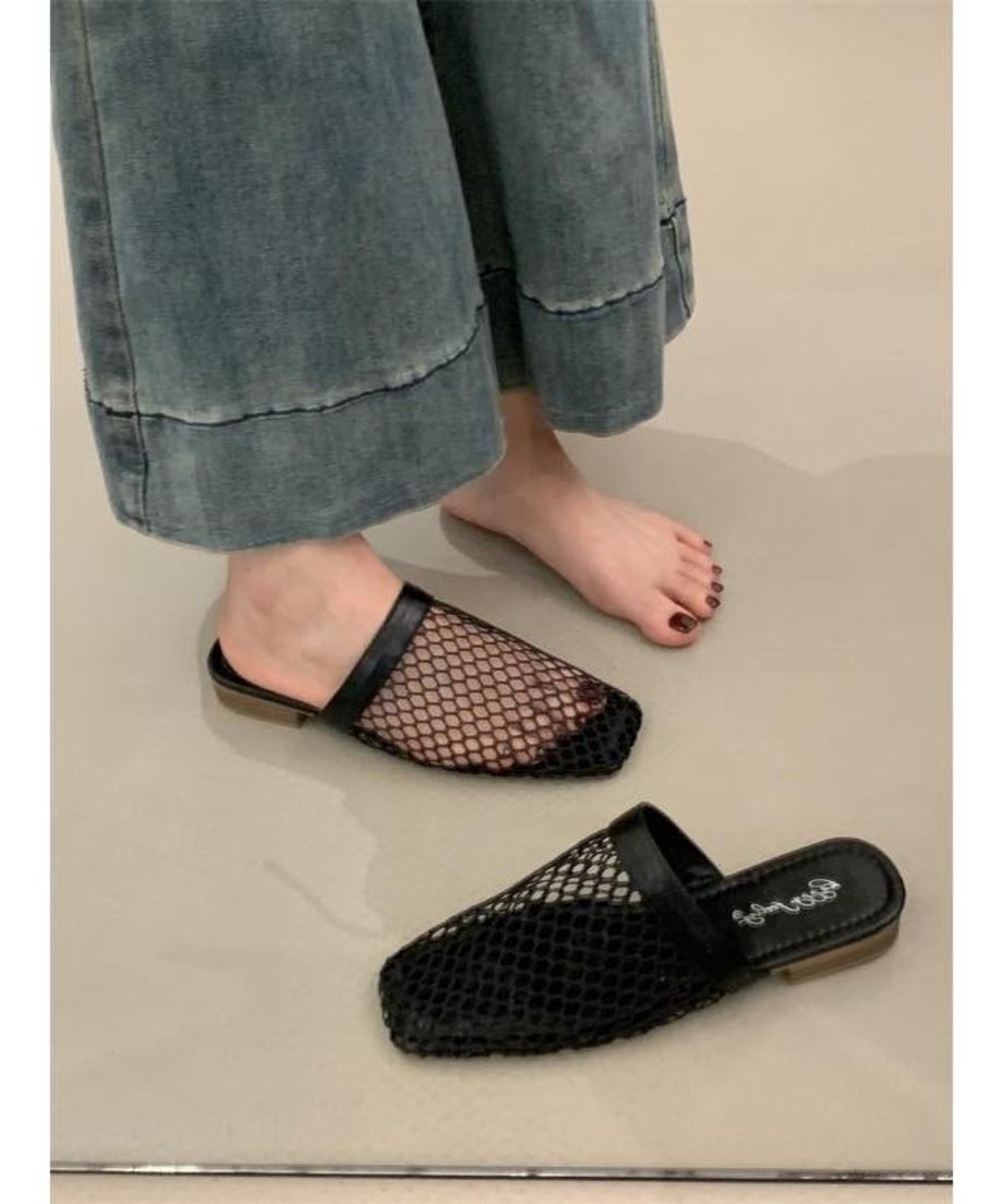 デニムのワイドパンツを着用した女性の足元。ブラックのスクエアトゥサンダルを片足履いており、もう一足は床に置かれている。