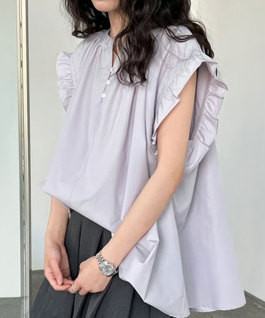女性がラベンダー色のフリルスリーブブラウスとダークグレーのスカートを着用している写真