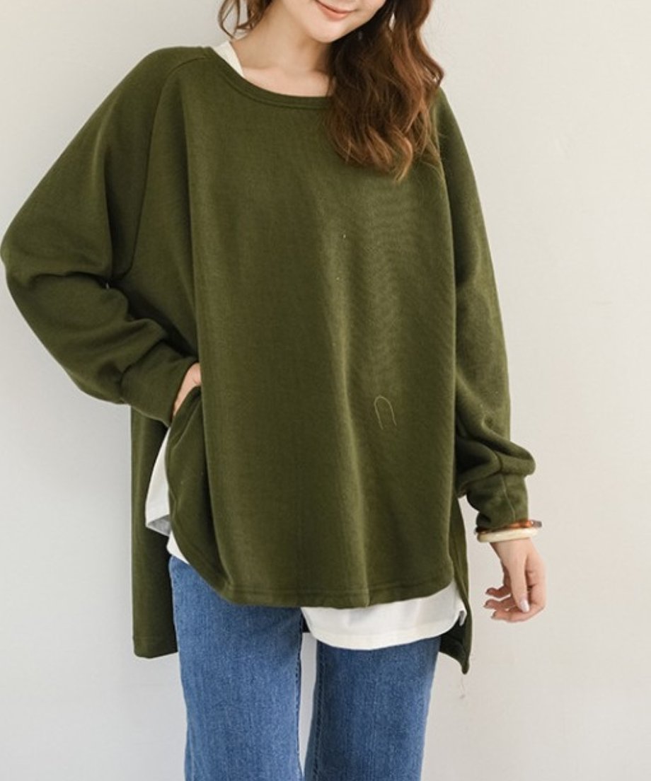 アーミーグリーンのオーバーサイズニットを着用した女性のバストアップ。白いTシャツをレイヤードし、デニムパンツを合わせたカジュアルな着こなし。