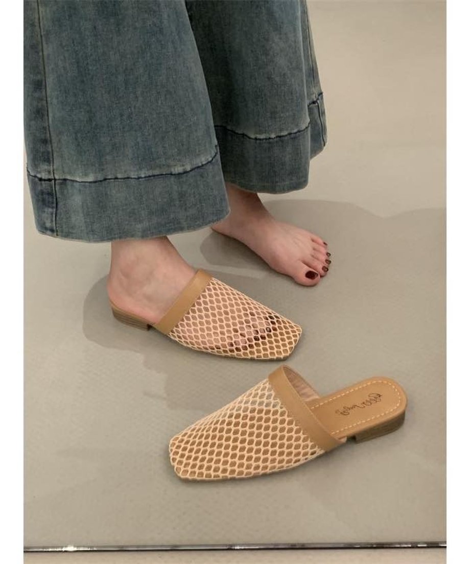 デニムのワイドパンツを着用した女性の足元。ベージュのスクエアトゥサンダルを片足履いており、もう一足は床に置かれている。