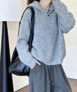 グレーのフード付きニットを着用し、同色のワイドパンツを合わせた女性の全身。黒いレザーの斜め掛けバッグを持っている。