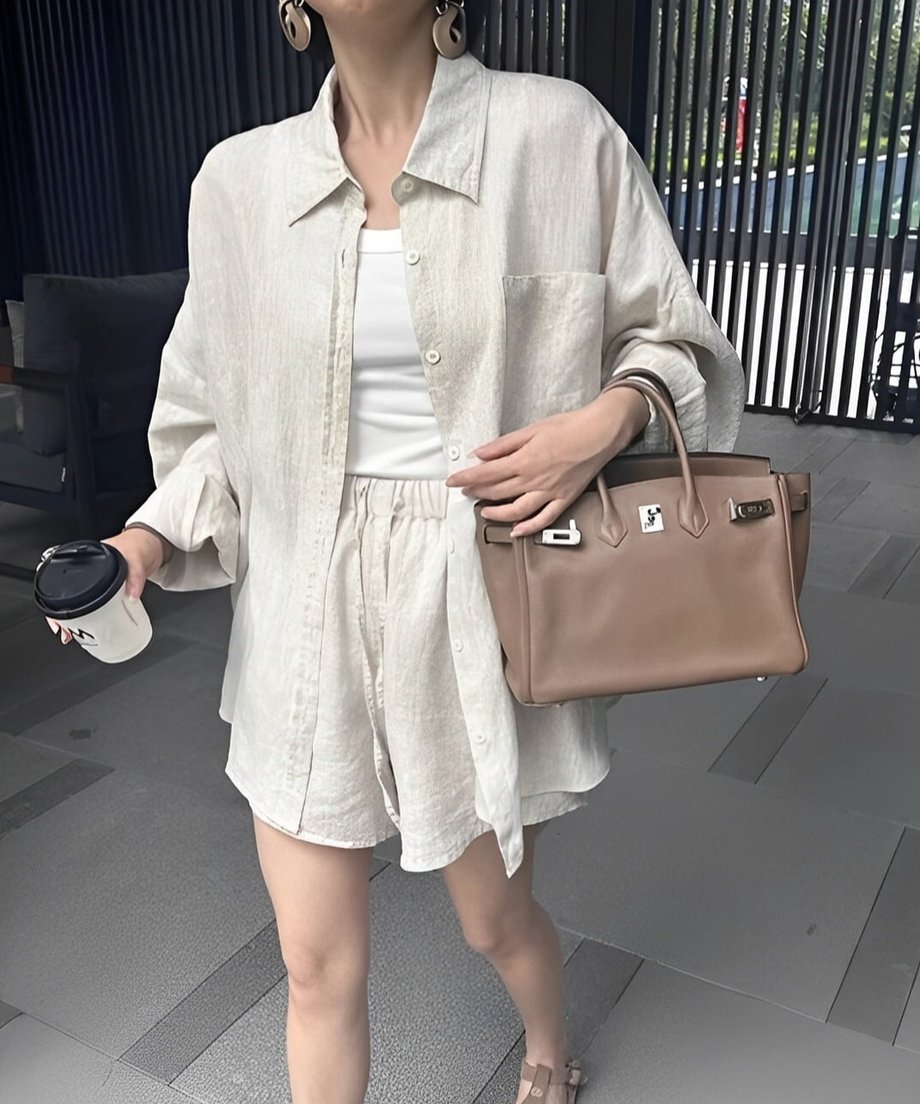 リネンのセットアップとショートパンツを着た女性がコーヒーカップを手に持っている。