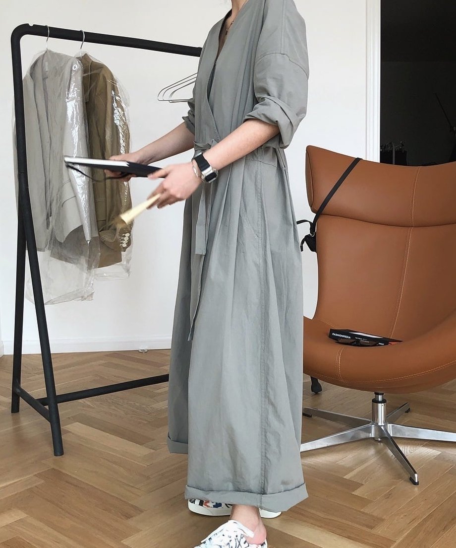 グレーのラップオールインワンを着用した女性が鏡越しに写る横向き全身ショット。