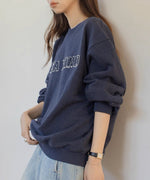 ネイビーのロゴスウェットシャツを着た女性が横向きに立っている姿。