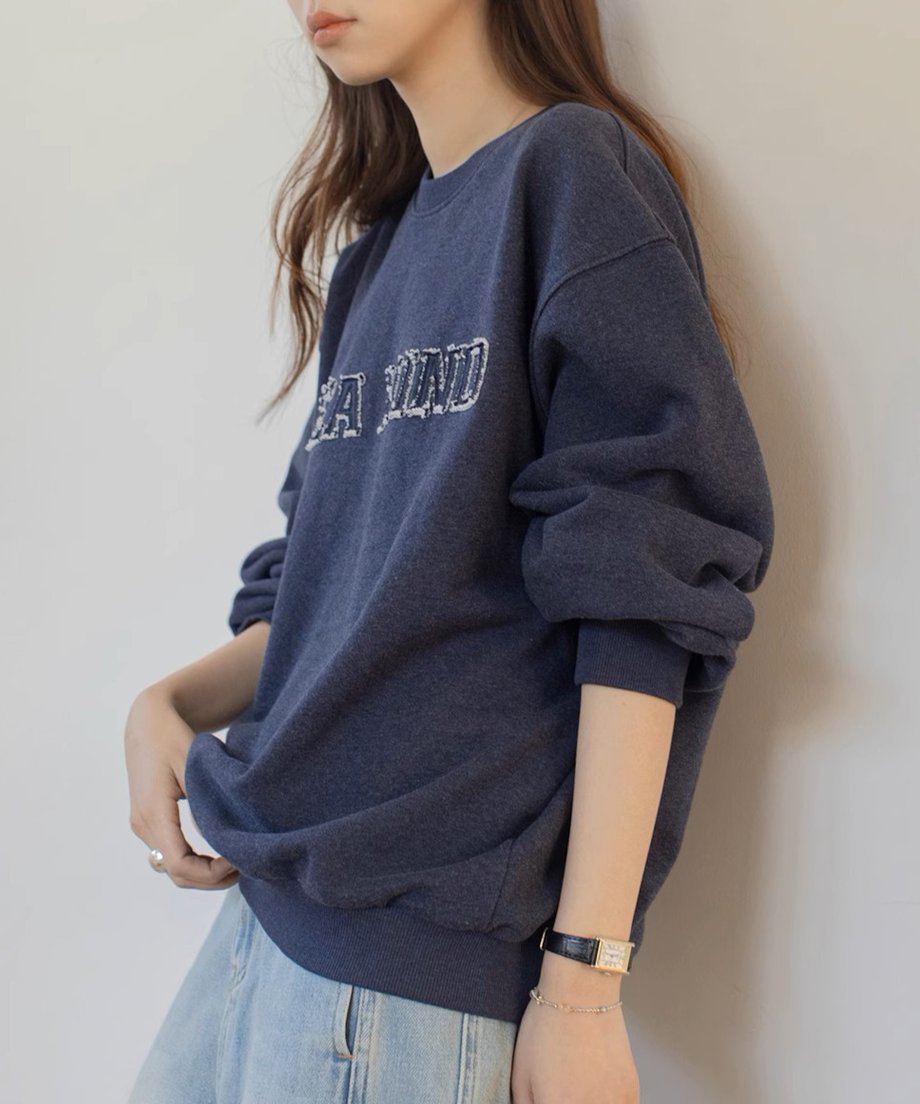 ネイビーのロゴスウェットシャツを着た女性が横向きに立っている姿。