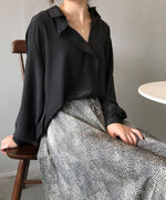 ランダムドット柄のロングテールスカートに黒のオーバーサイズシャツを着た女性が、木製の椅子に座っている上半身。