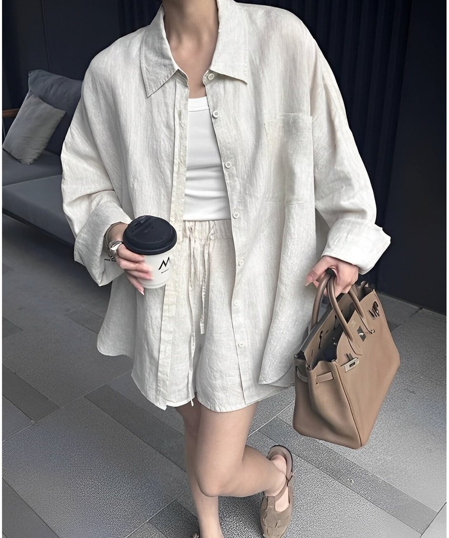 リネンのセットアップを着た女性がバッグとコーヒーカップを持っている。