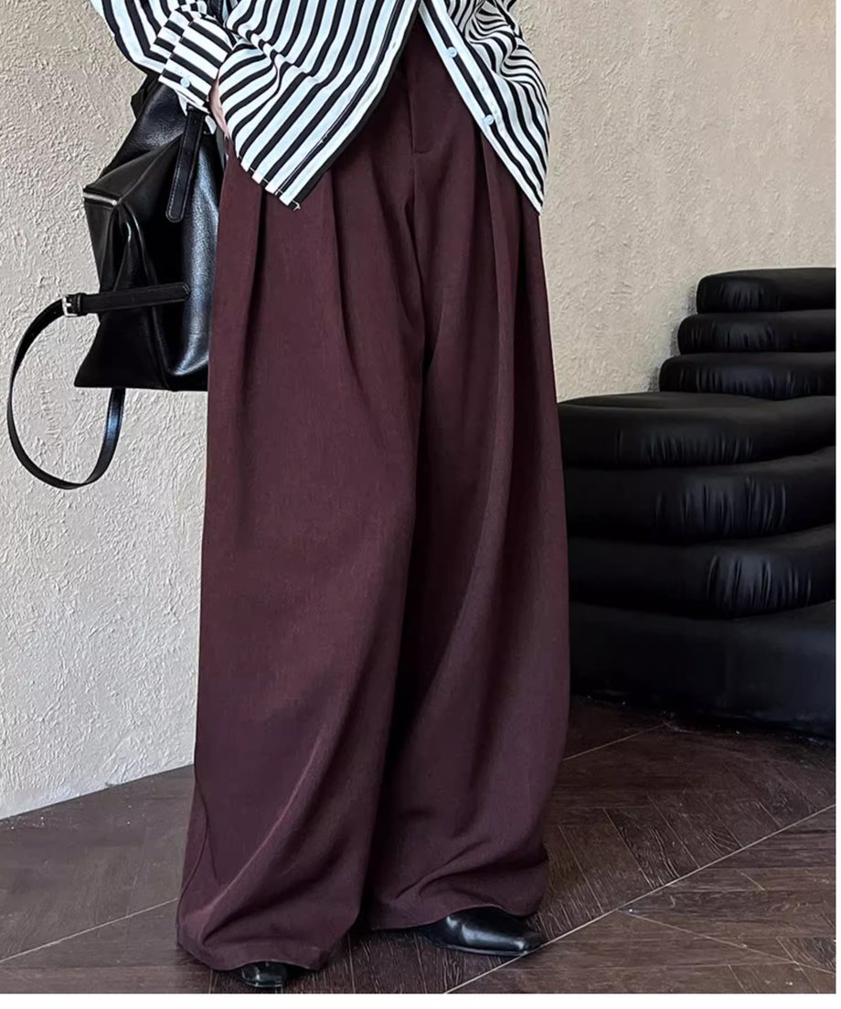 ボルドーのワイドパンツを着用した女性の全身。ストライプのシャツを合わせており、パンツの深いタックとボリューム感が際立つ。