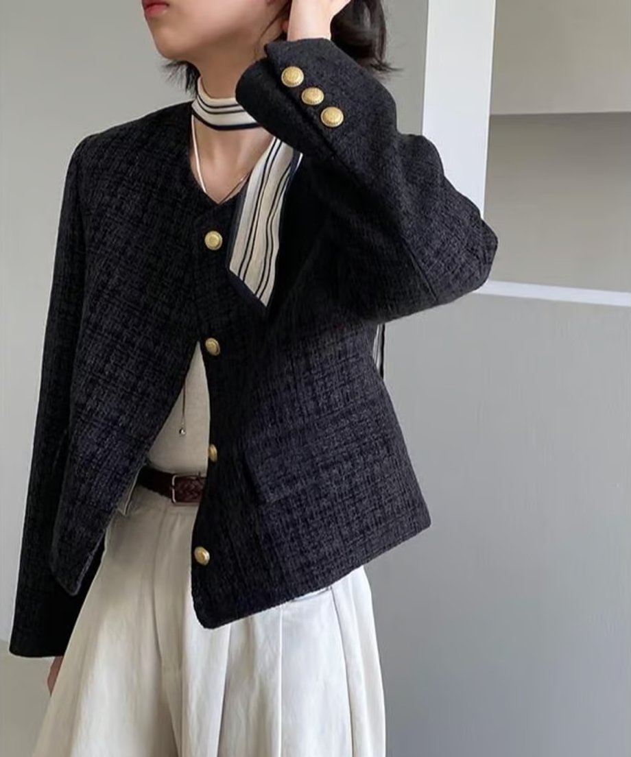 黒のツイード風ジャケットにオフホワイトのワイドパンツを合わせた女性が立っている姿。