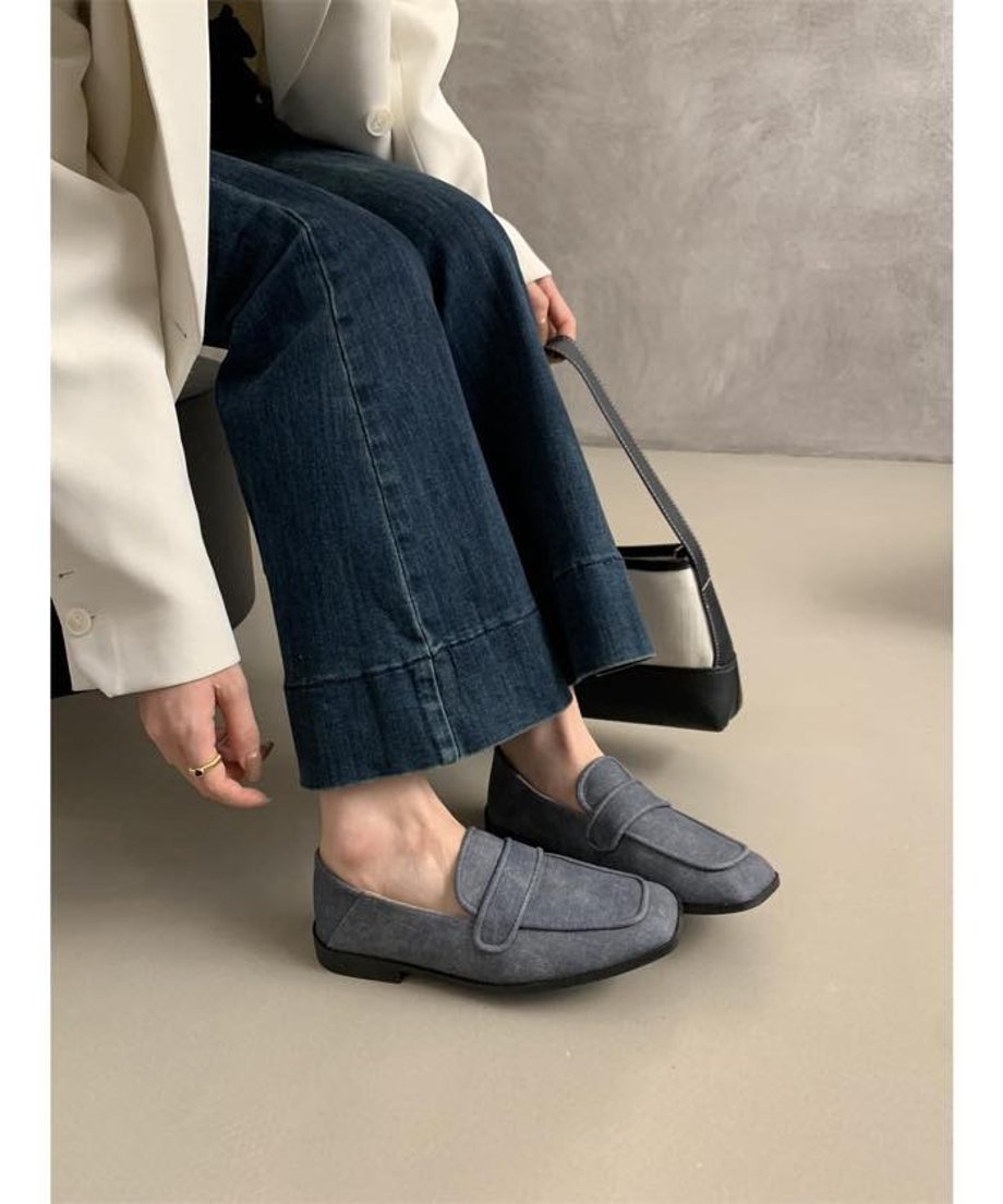 デニムグレーのキャンバス製スクエアトゥローファーを着用した女性の足元。濃紺のデニムパンツと白のジャケットと合わせて座っている。