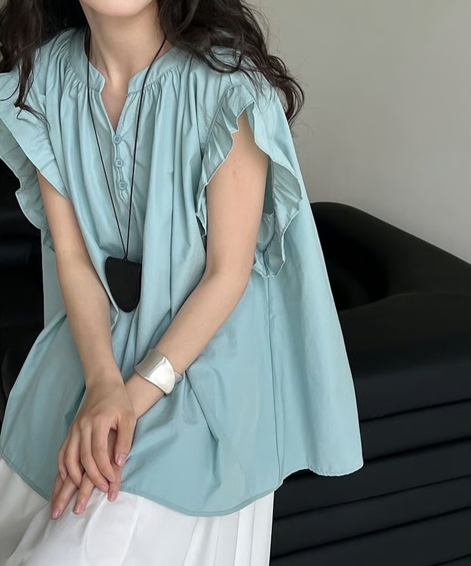 女性がライトブルーのブラウスを着用し、座ってネックレスを合わせている写真