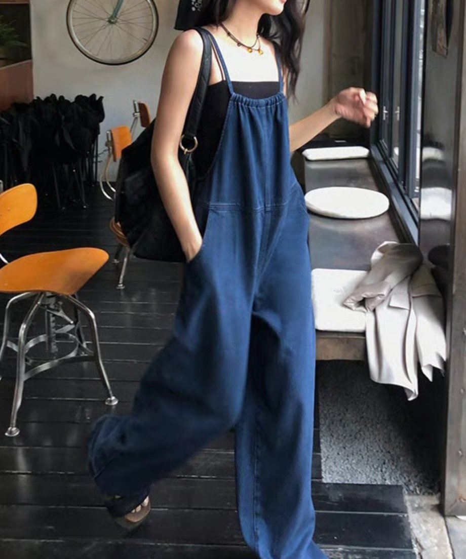 ブラックのタンクトップとデニムサロペットを着た女性が、カフェの中を歩いている。