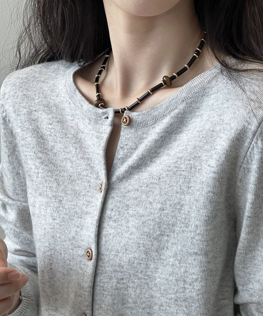 グレーのクルーネックカーディガンを着用した女性のクローズアップ。黒と茶色のビーズネックレスを着用している。