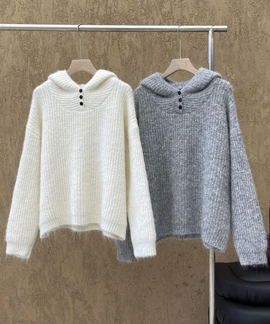 白いハンガーに掛けられたオフホワイトとグレーの2色のフード付きニットの正面平置き画像。