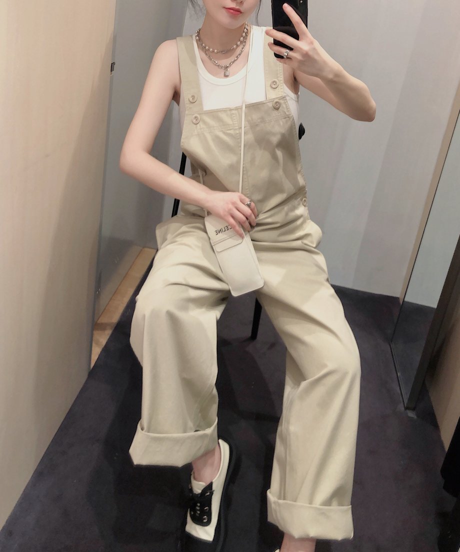カーキのオーバーオールを着用した人物が椅子に座って足を崩している。