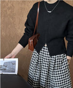 ブラックのハーフジップニットと白黒チェックのロングスカートを着用した女性の胸元。茶色のバッグを肩に掛けている。