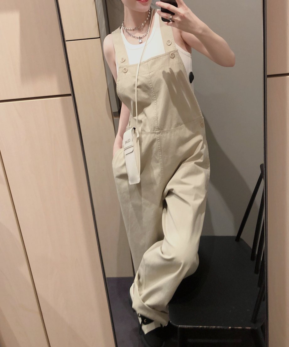 カーキのオーバーオールを着用した人物が鏡の前でポーズをとっている。