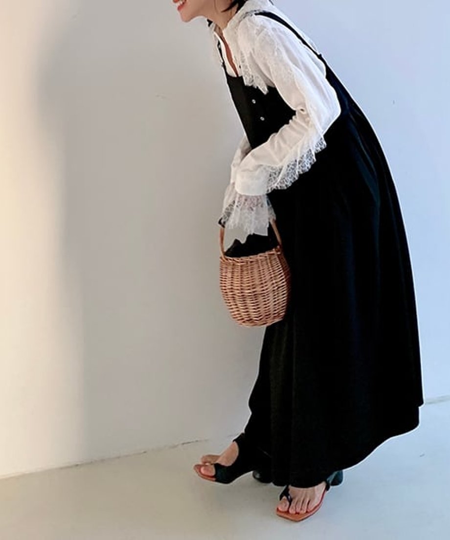 黒のサスペンダーロングワンピースに白いフリル襟の半袖Tシャツをインナーにした女性の前屈みショット。