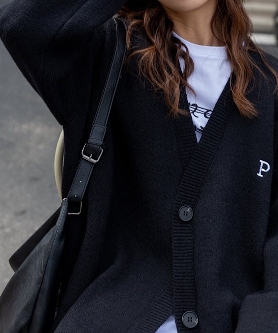 黒いオーバーサイズカーディガンの左胸にある白い「P」の刺繍ロゴとボタンをクローズアップした写真。