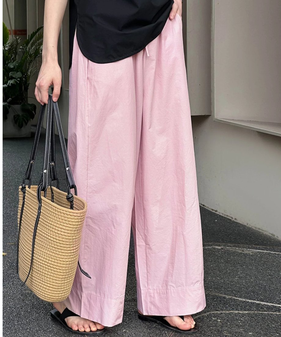 ピンクのワイドレッグパンツと黒のノースリーブを着用し、ナチュラルな編みバッグを持った、足元のクローズアップ写真