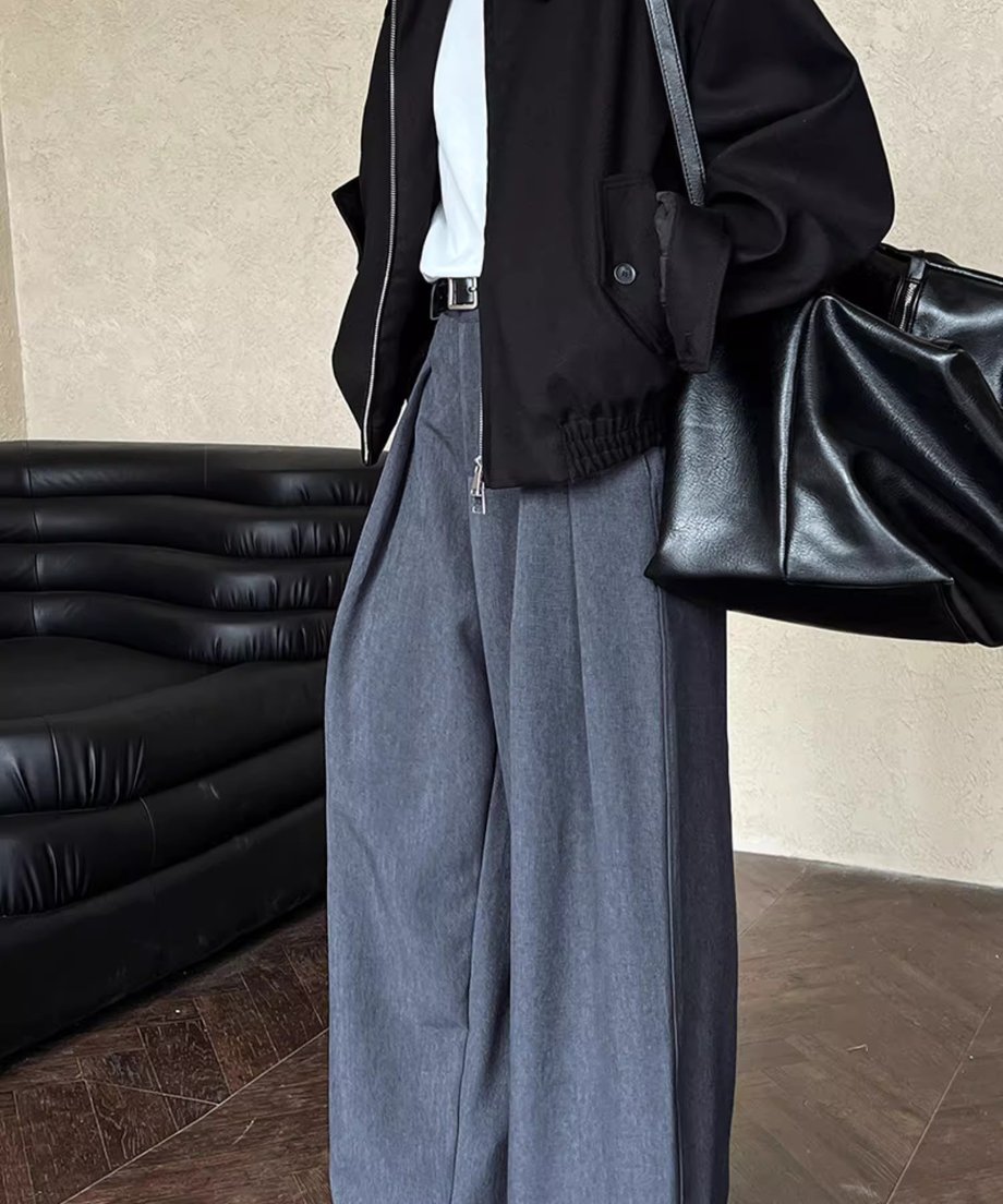 グレーのタックワイドパンツを着用した女性の全身。黒いブルゾンとバッグを合わせたマニッシュなスタイル。