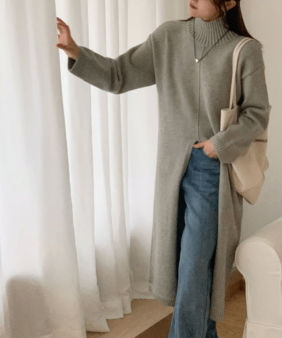 ライトグレーのタートルネックロングニットを着用した女性が、青いデニムパンツをレイヤードしたスタイル。