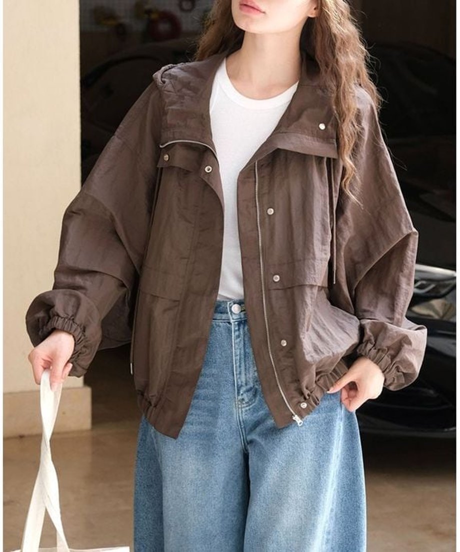ブラウンのフードブルゾンを着用し、淡いデニムパンツと合わせた女性の正面からの写真。ジッパーを開けて白Tシャツを見せている。