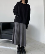 ブラックのボリュームスウェットに、グレーのロング丈プリーツスカートを合わせ、黒いスニーカーを履いた女性の全身写真。