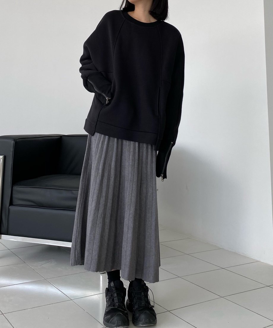 ブラックのボリュームスウェットに、グレーのロング丈プリーツスカートを合わせ、黒いスニーカーを履いた女性の全身写真。